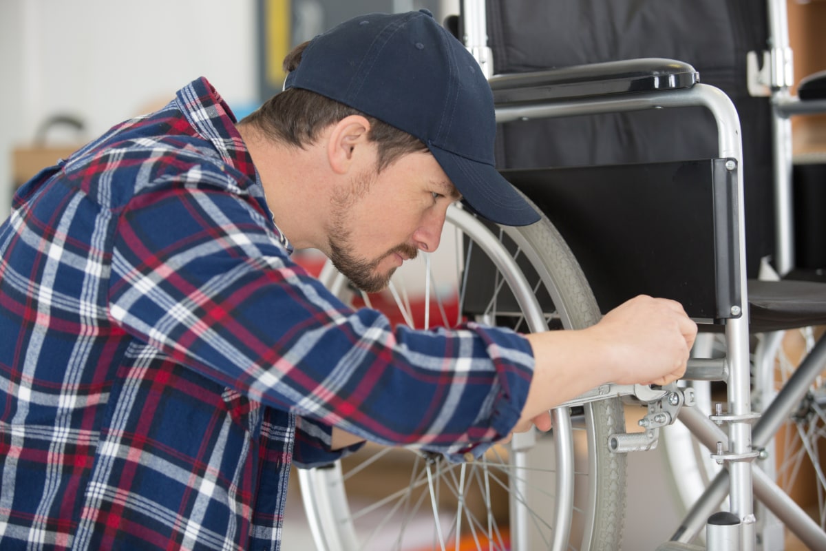 man in plaid wearing a baseball hat repairing a wheelchair