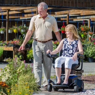 woman sitting in a power wheelchair and man standing next to her pointing at flowers in a nursery